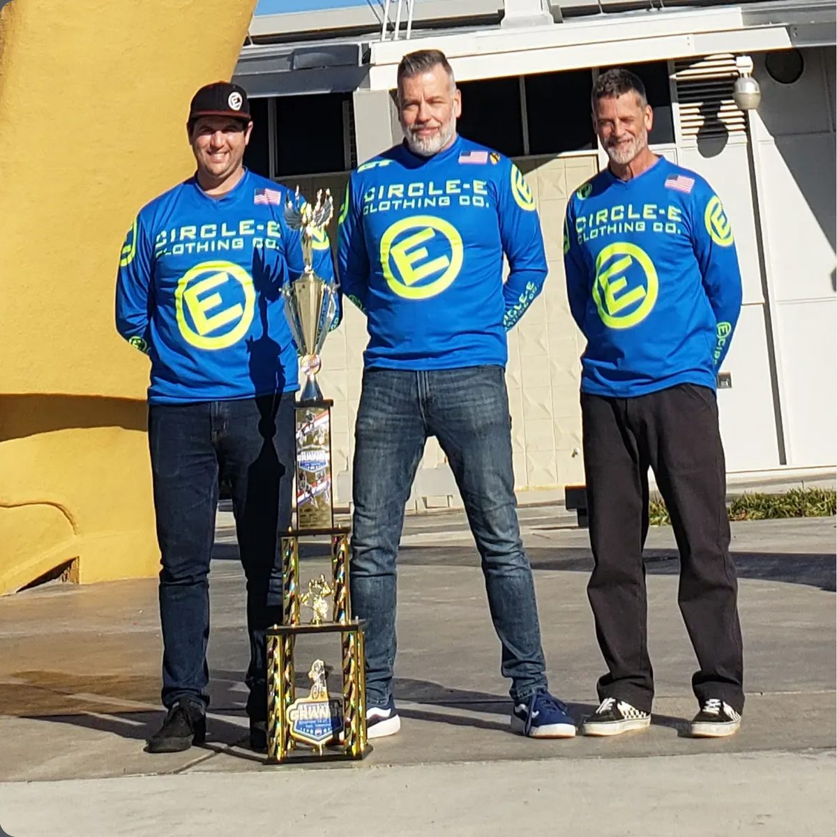 Three riders in Circle-E jerseys beside a trophy